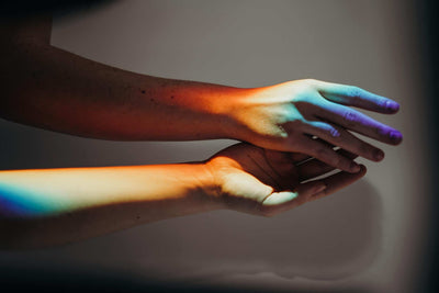 two hands touching with a rainbow light shining down