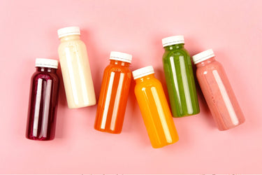 bottles of different colored smoothies on a pink background