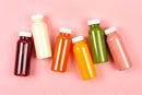 bottles of different colored smoothies on a pink background