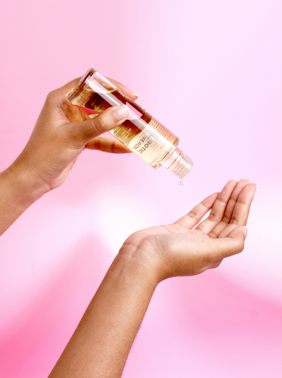 pouring massage oil into hand on a pink background