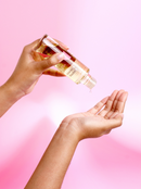 pouring massage oil into hand on a pink background